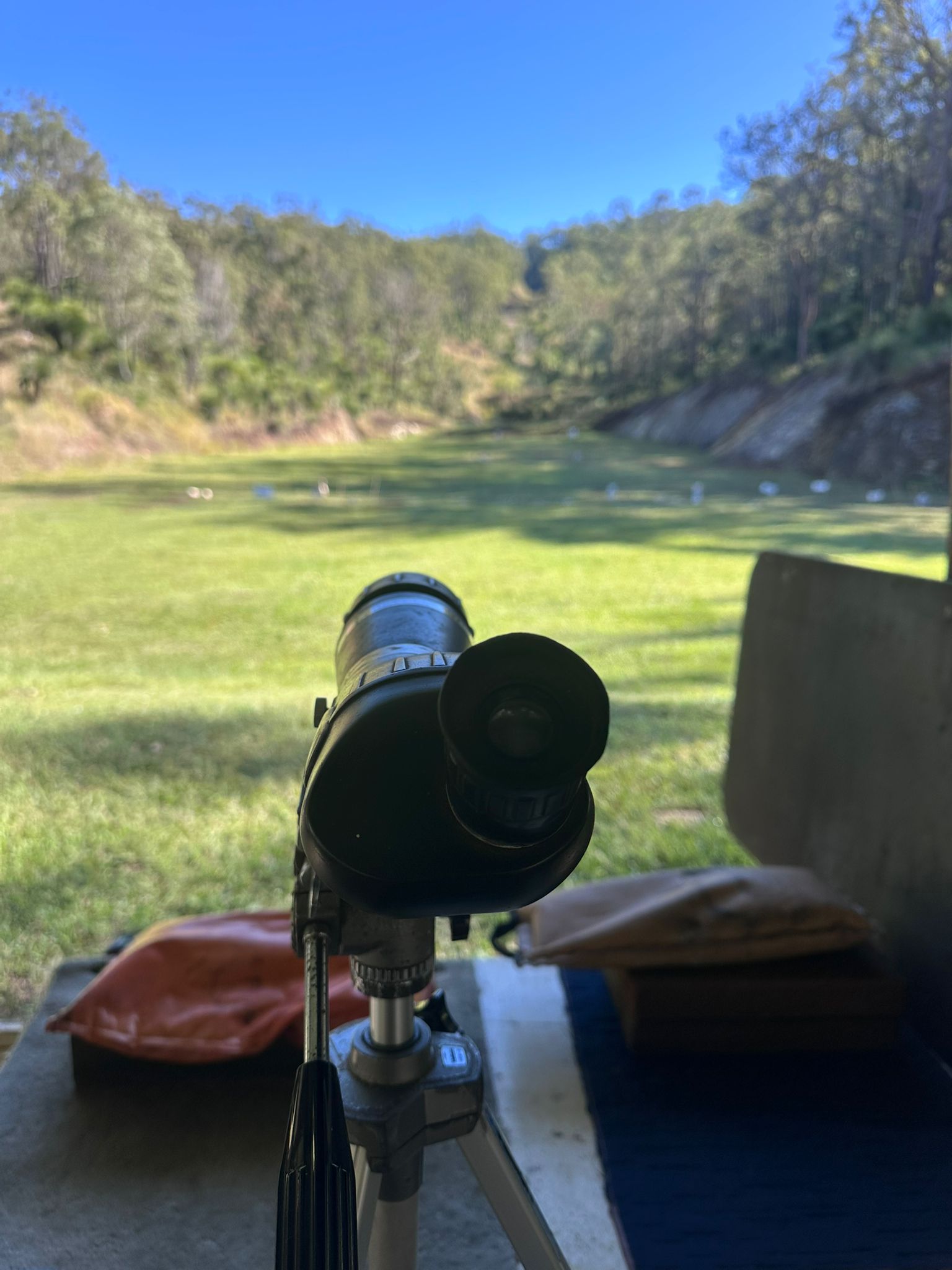 A scoped rifle resting on the bench with the 300m range beyond at Wattle Grove Park